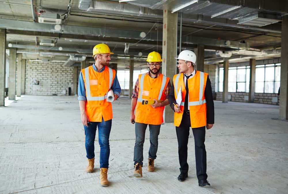 Group Of Contractors Walking Down Concrete Floor Of Unfinished Construction
